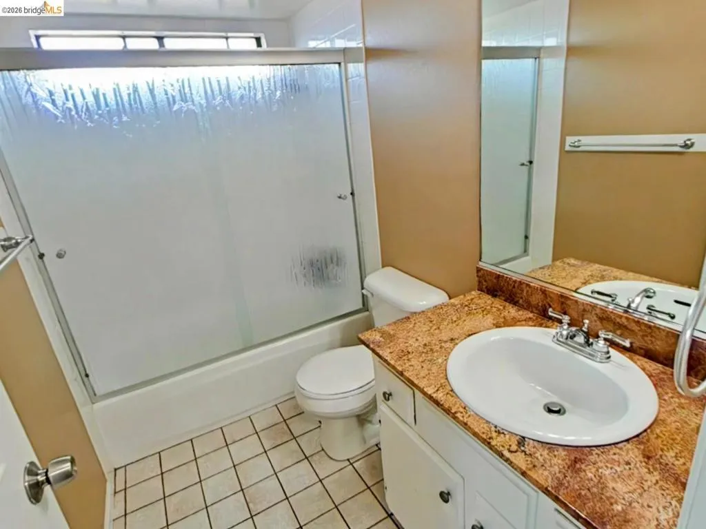 Bathroom featuring a white vanity with an oval sink, a speckled countertop, a large wall mirror, and a full-size bathtub with a sliding frosted glass enclosure