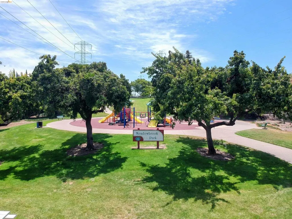 Community park featuring a dedicated play area with colorful structures, surrounded by mature trees providing natural shade