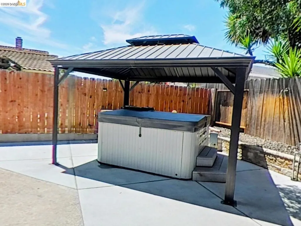 Hot tub with a protective cover situated under a metal-roofed gazebo on a concrete patio