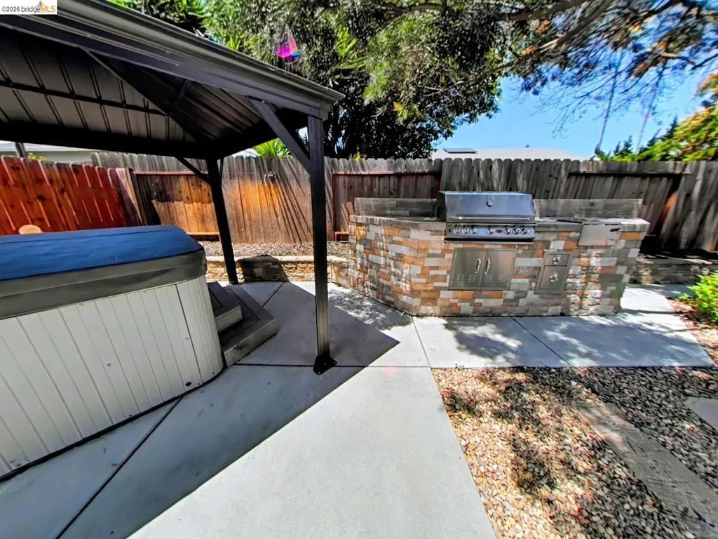 Outdoor living area with a stone-clad built-in BBQ station, stainless steel appliances, and a covered hot tub