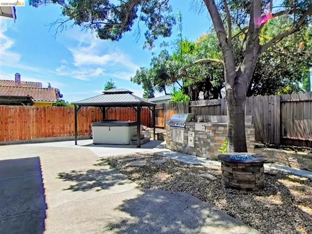 Expansive backyard featuring a stone-clad outdoor kitchen with built-in grill, a covered spa area, and a stone fire pit