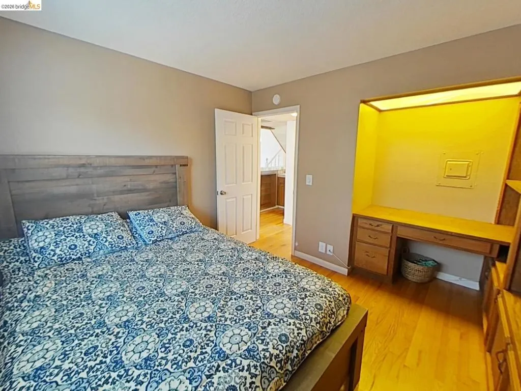 Hardwood flooring throughout featuring a built-in illuminated desk with integrated storage, a light wood-finish headboard, and neutral wall paint