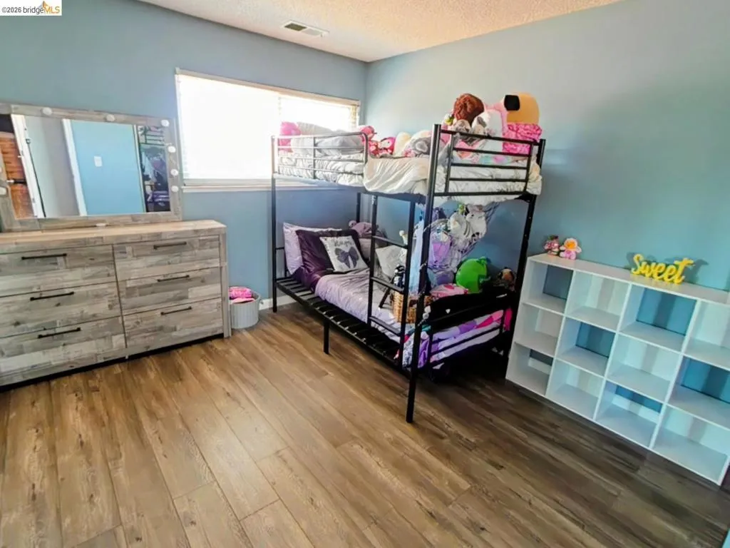 Spacious room featuring wood-finish flooring, a large window, light blue wall paint, and recessed lighting