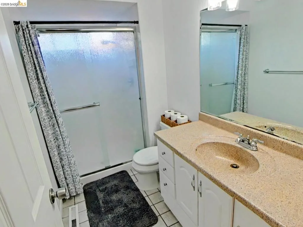 Full bathroom featuring a shower with a sliding frosted glass door, a toilet, a vanity with a speckled countertop and integrated sink, a chrome faucet, and a large mirror
