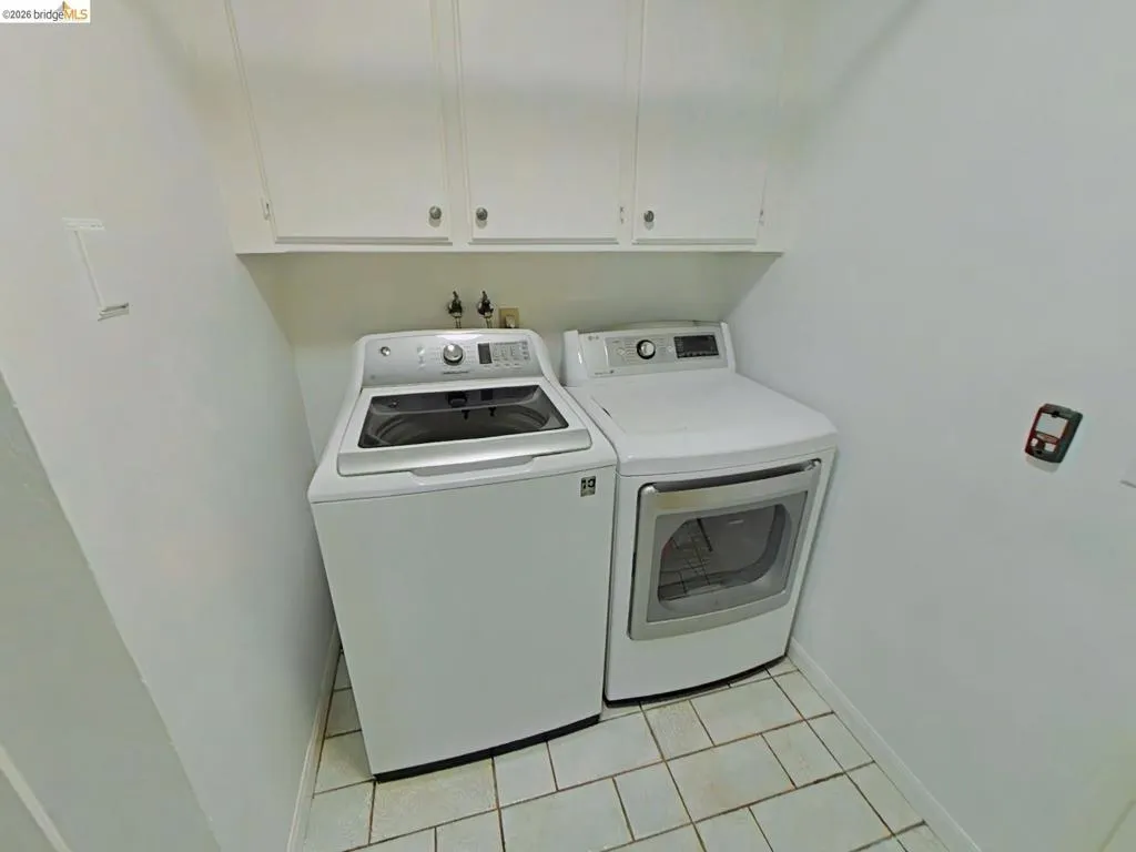 Dedicated laundry area featuring overhead white cabinetry and tile flooring