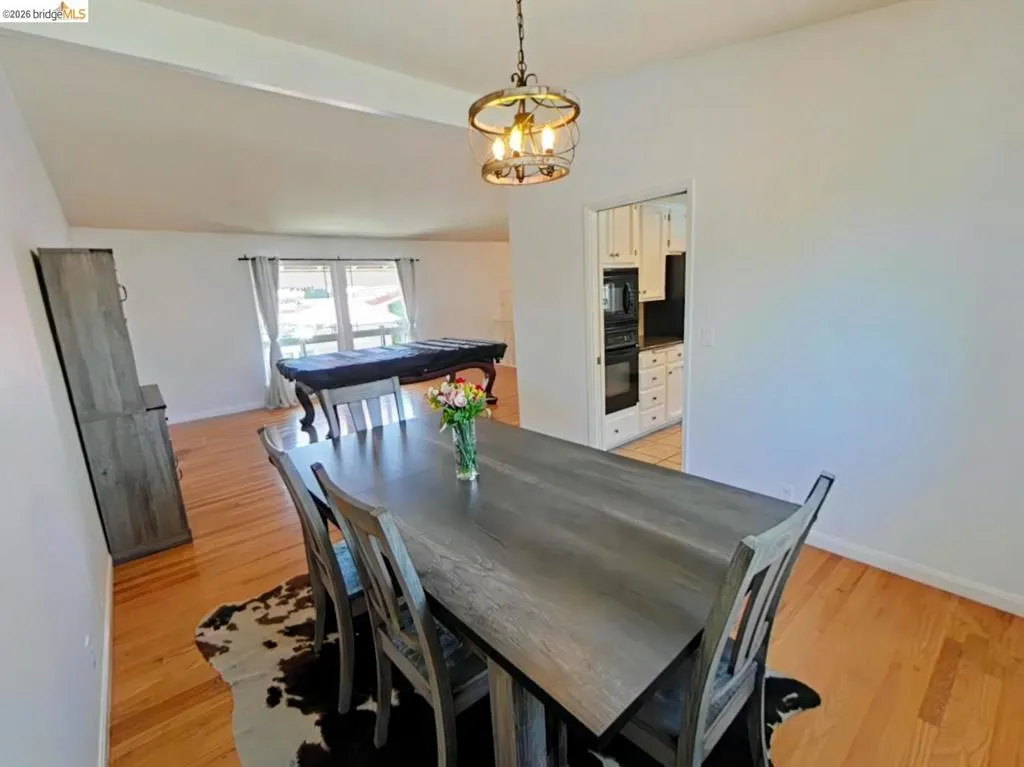 Dining area with wood-finish flooring, featuring a decorative chandelier and a pass-through opening to the kitchen