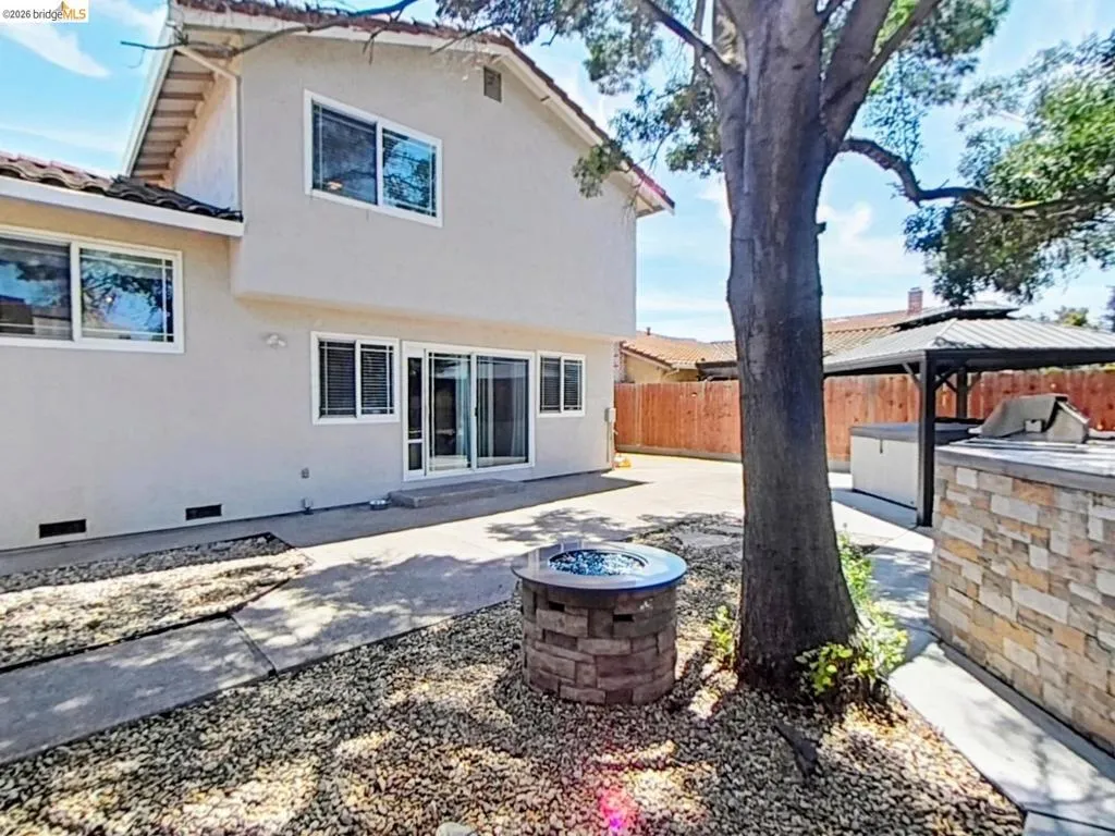 Backyard featuring a stone-clad fire pit, concrete patio, and a covered outdoor kitchen area with stone finishes