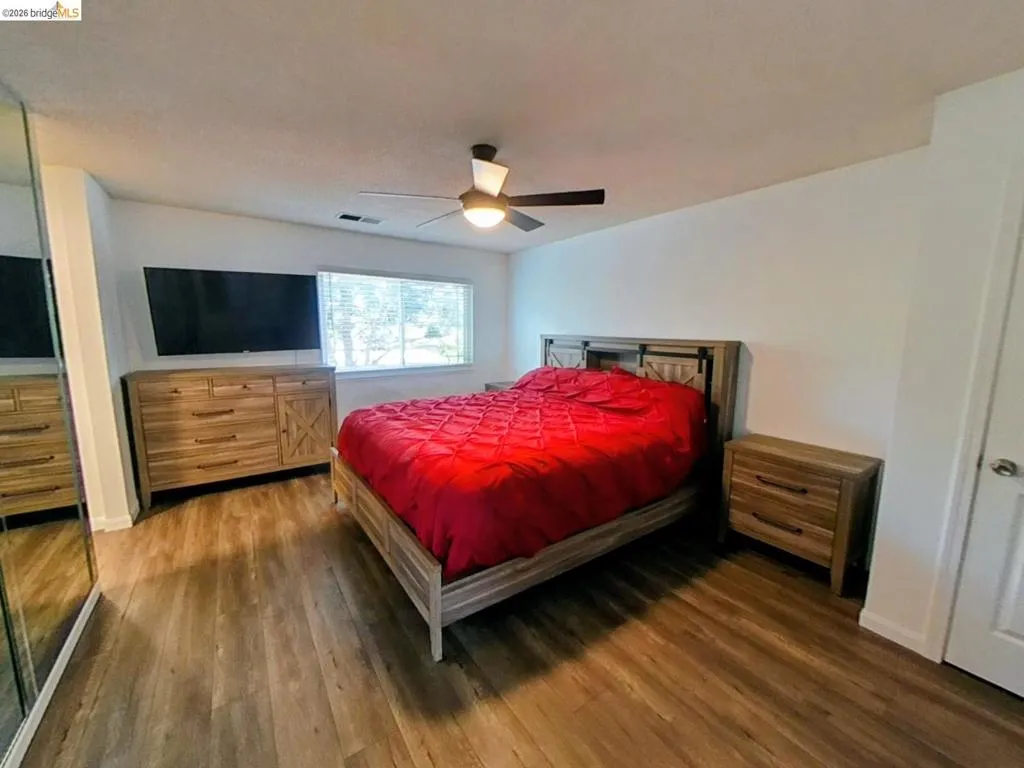 Primary bedroom featuring wood-finish flooring, a ceiling fan with integrated lighting, a wide window with blinds, and a built-in mirrored closet