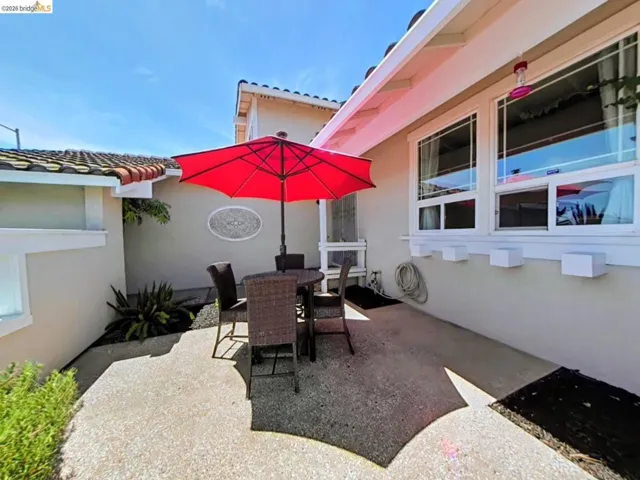 Concrete patio featuring a decorative wall accent, low-maintenance landscaping, and traditional tile roofing