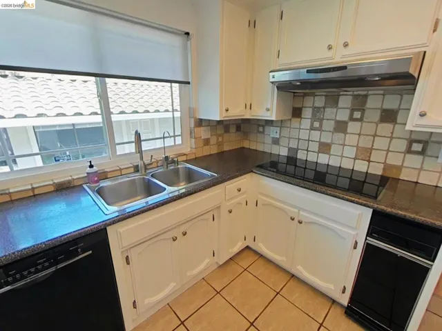Kitchen featuring white cabinetry, a double basin stainless steel sink, dark speckled countertops, a mosaic tile backsplash, and tile flooring
