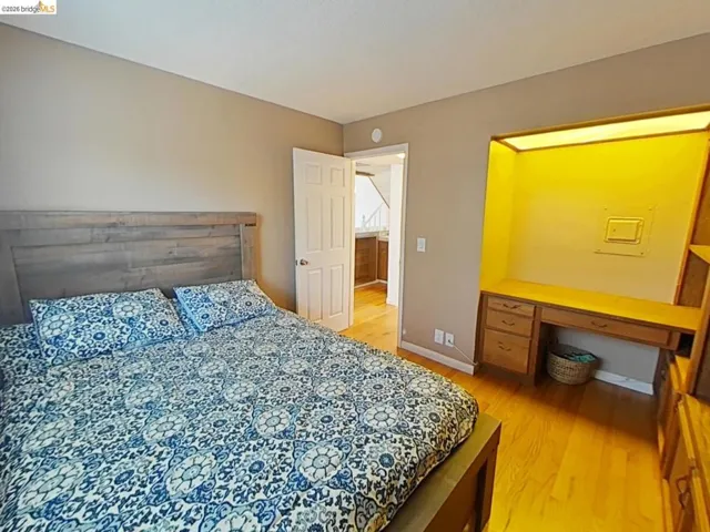 Hardwood flooring throughout featuring a built-in illuminated desk with integrated storage, a light wood-finish headboard, and neutral wall paint