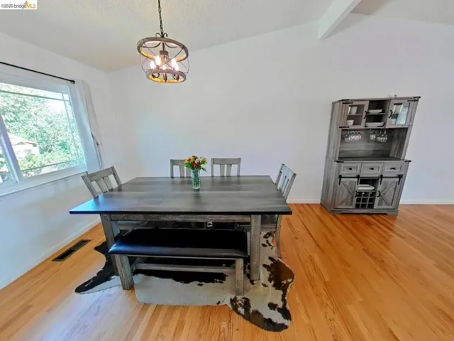 Spacious room featuring vaulted ceilings, a prominent window, a decorative ceiling light fixture, and wood-finish flooring