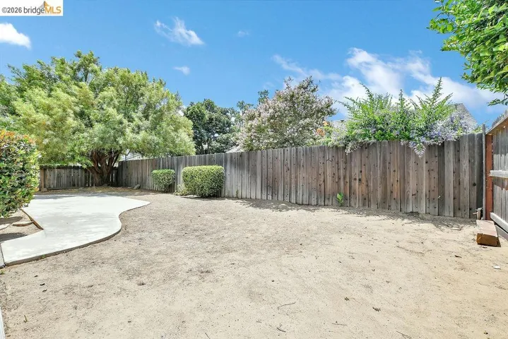 Spacious backyard featuring a large concrete patio, wood privacy fencing, and mature trees providing natural shade