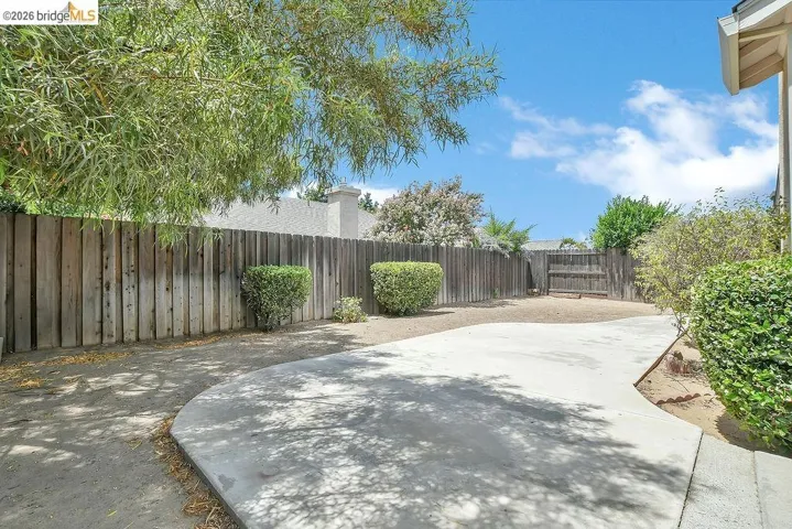Private backyard featuring a wooden fence, concrete patio, and established shrubbery