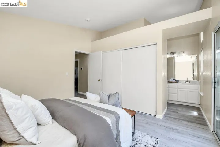 Bedroom featuring wood-finish flooring, neutral wall tones, a sliding closet door, and an entryway to a full bathroom with a single vanity