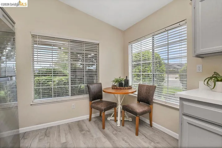 Corner dining nook featuring two large windows with horizontal blinds, light wood-finish flooring, and a vaulted ceiling