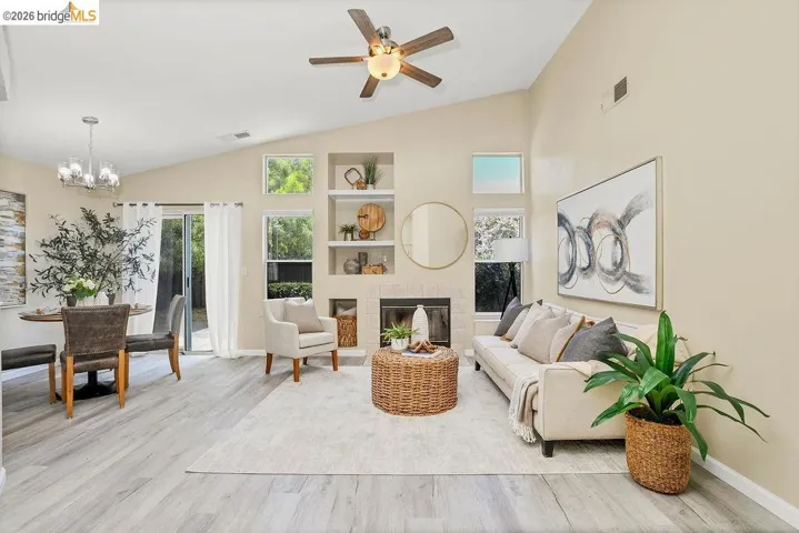Vaulted ceilings enhance this open-concept living space featuring wood-finish flooring, a built-in shelving unit, and a contemporary ceiling fan