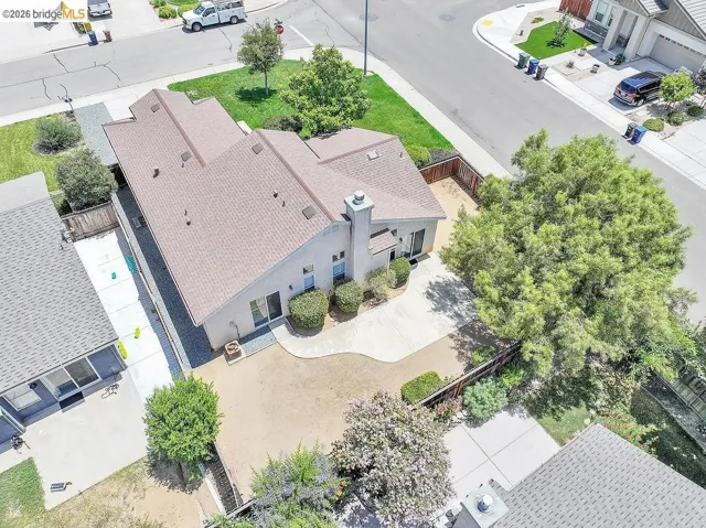 Aerial perspective highlighting the property's roofline, a paved patio area, and mature perimeter landscaping