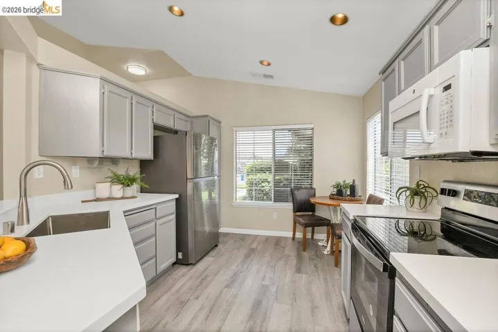 Kitchen featuring light gray cabinetry, white countertops, stainless steel appliances, and wood-finish flooring