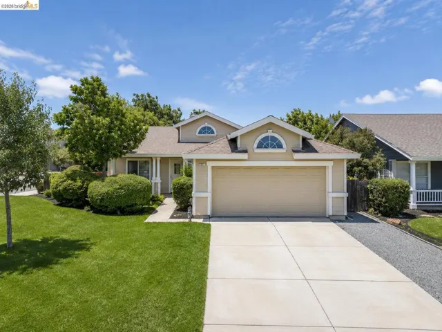 Single-story home featuring a two-car garage, mature landscaping, and an arched transom window