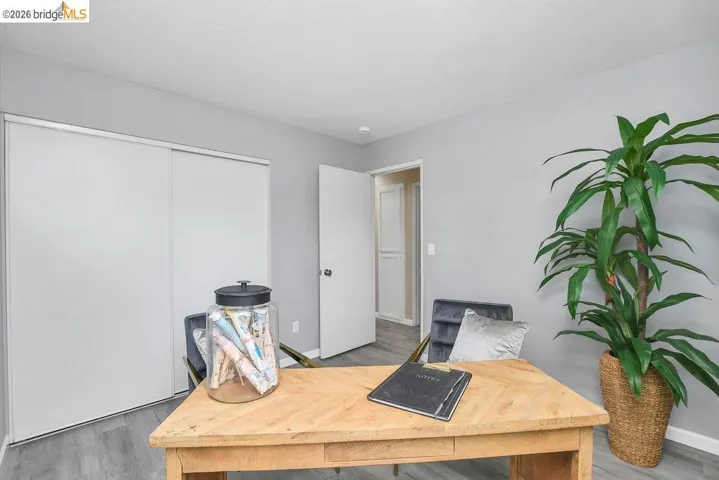 Light gray walls complement the wood-finish flooring in this room featuring a wooden desk, white sliding closet doors, and a white interior door