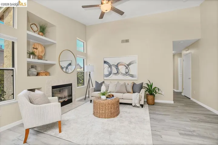 Living space featuring high ceilings, wood-finish flooring, a ceiling fan with integrated lighting, a fireplace with a stone surround, and built-in shelving