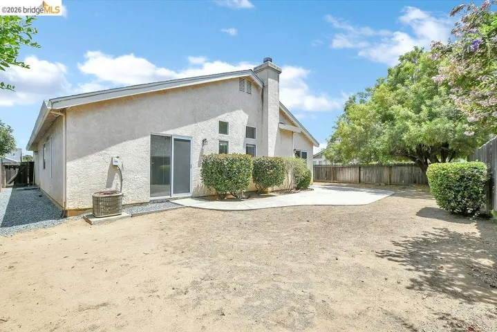 Rear exterior featuring stucco siding, a concrete patio, and mature perimeter trees