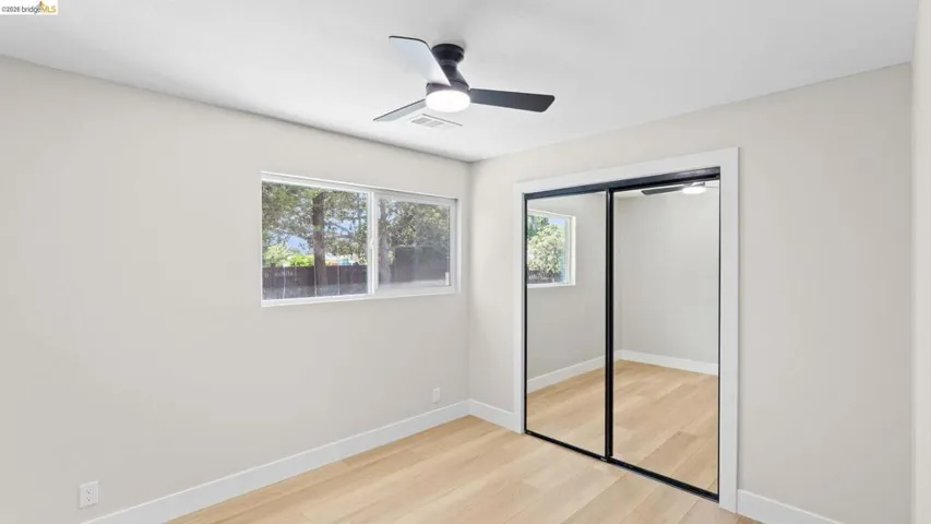 Spacious room featuring wood-finish flooring, a modern ceiling fan, and large mirrored closet doors