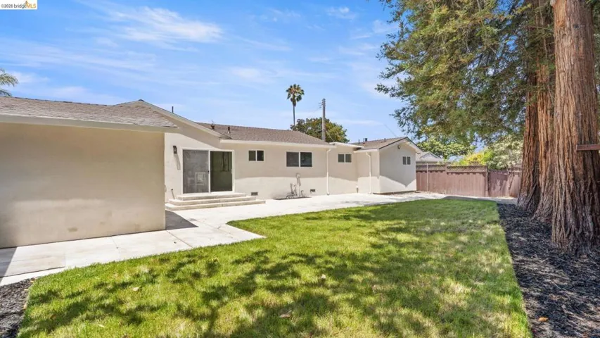 Expansive backyard featuring a manicured lawn, established trees, concrete patio, and a privacy fence