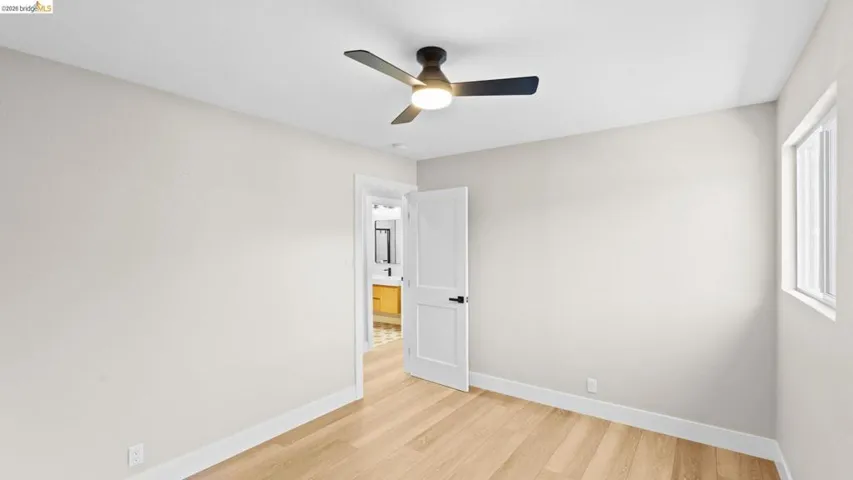 Bright interior space featuring light wood-finish flooring, a contemporary ceiling fan with integrated lighting, and a white interior door with matte black hardware