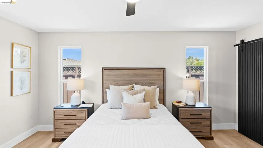 Bedroom featuring light-toned walls, two framed windows, wood-finish flooring, and a black barn door