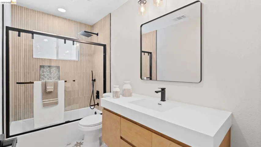 Modern bathroom featuring a wood-finish floating vanity with an integrated white sink, matte black faucet, and a large framed mirror