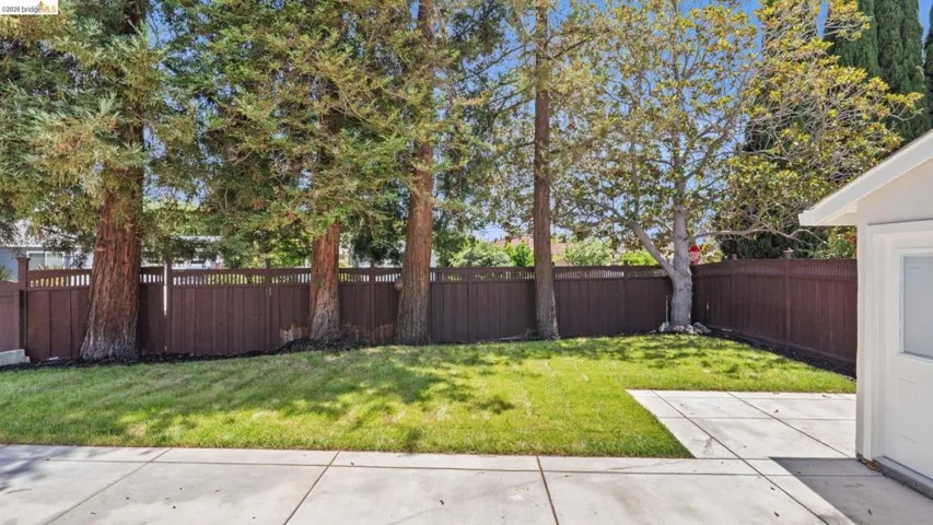 Expansive backyard featuring a manicured lawn, established trees, and a durable wood fence