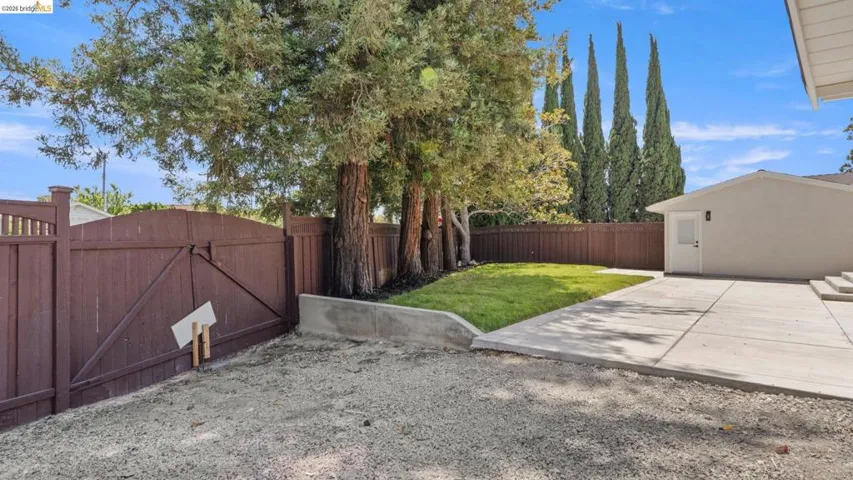 Expansive exterior featuring a brown privacy fence, mature trees, and a gravel surface