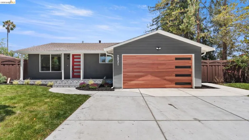 Contemporary exterior featuring a vibrant red entry door, a wood-finish garage door, dark gray siding, a patterned tile porch, and a concrete driveway