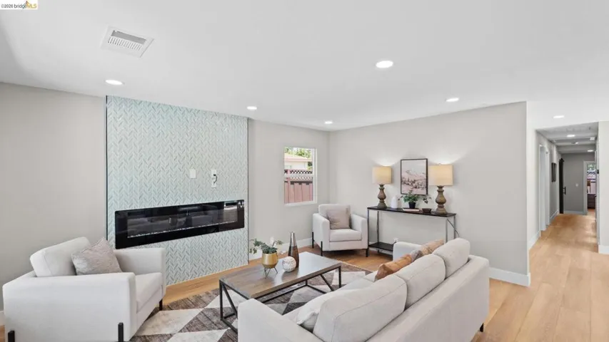 Living area featuring an accent wall with a linear electric fireplace, recessed lighting, light wood-finish flooring, and crisp white baseboards