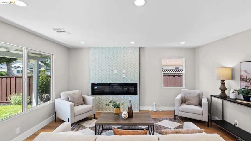 Contemporary living area featuring wood-finish flooring, recessed lighting, and a textured accent wall with a linear electric fireplace