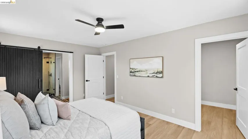 Bedroom featuring a black barn door, light wood-finish flooring, a modern black ceiling fan, white baseboards, and white interior doors with black hardware