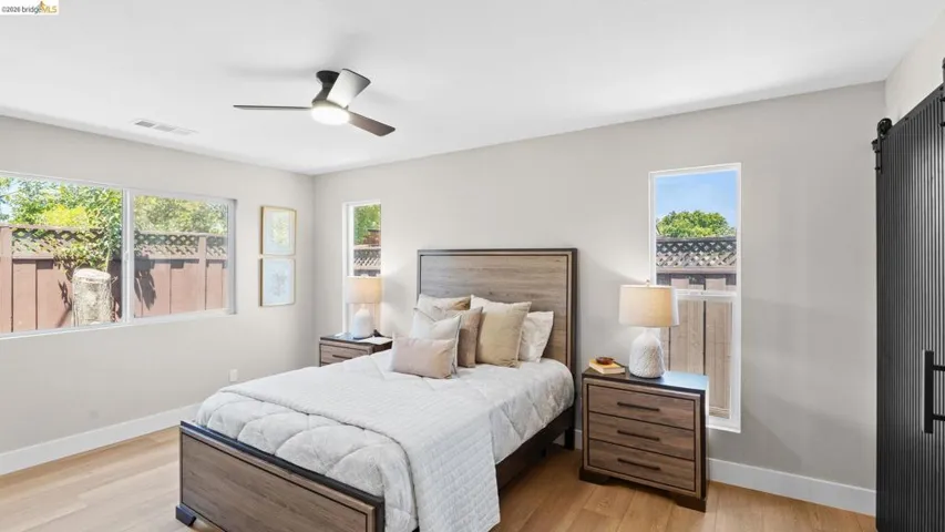 Bedroom featuring light wood-finish flooring, multiple windows, a ceiling fan with integrated lighting, and a dark wood-finish sliding barn door
