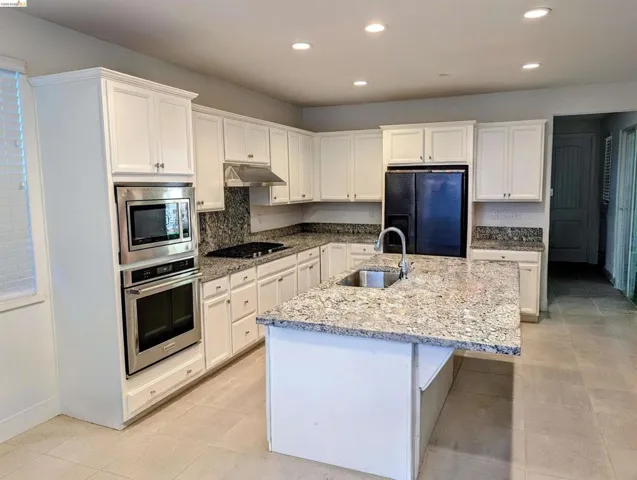 Kitchen featuring white cabinetry, granite countertops, stainless steel appliances, a center island with an undermount sink, and recessed lighting