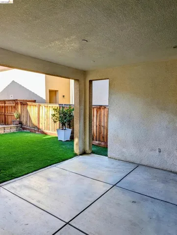 Covered patio featuring concrete flooring with expansion joints, stucco walls, and a synthetic turf lawn
