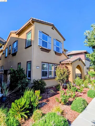 Two-story stucco exterior with decorative shutters, arched entry, and a well-maintained garden with various plantings