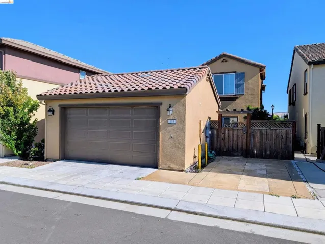 Stucco exterior featuring a two-car garage with a panel door, a tiled roof, and an additional paved parking area