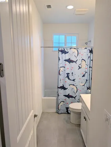 Bathroom featuring a built-in tub with shower, white vanity with integrated sink, and gray tile flooring
