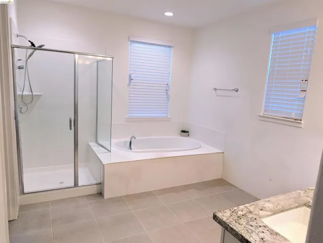 Spacious bathroom featuring a built-in soaking tub with a surrounding deck, a glass-enclosed shower, and a vanity with a stone countertop