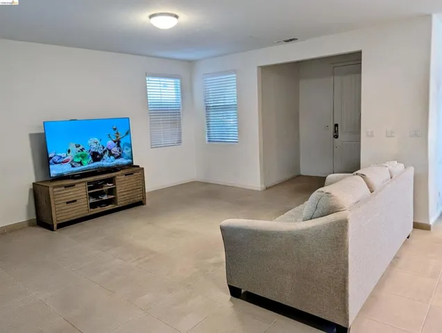 Spacious living area featuring large format tile flooring, neutral wall tones, and two windows with horizontal blinds