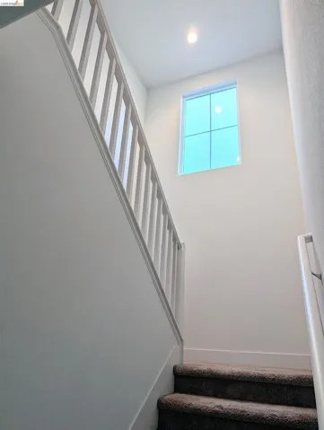 Carpeted staircase with white balusters and a square window