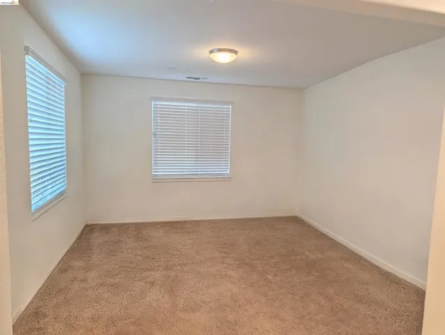 Carpeted room with two windows featuring blinds, a flush-mount ceiling light fixture, and white painted walls
