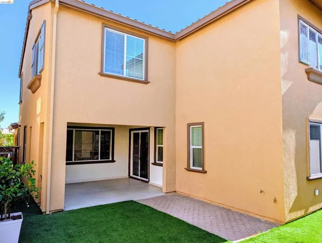 Rear exterior featuring a covered patio, artificial turf, and paver stone hardscaping