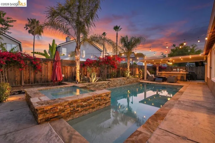 Private backyard oasis featuring a stone-faced spa, a swimming pool with stone coping, and a covered patio with an outdoor bar